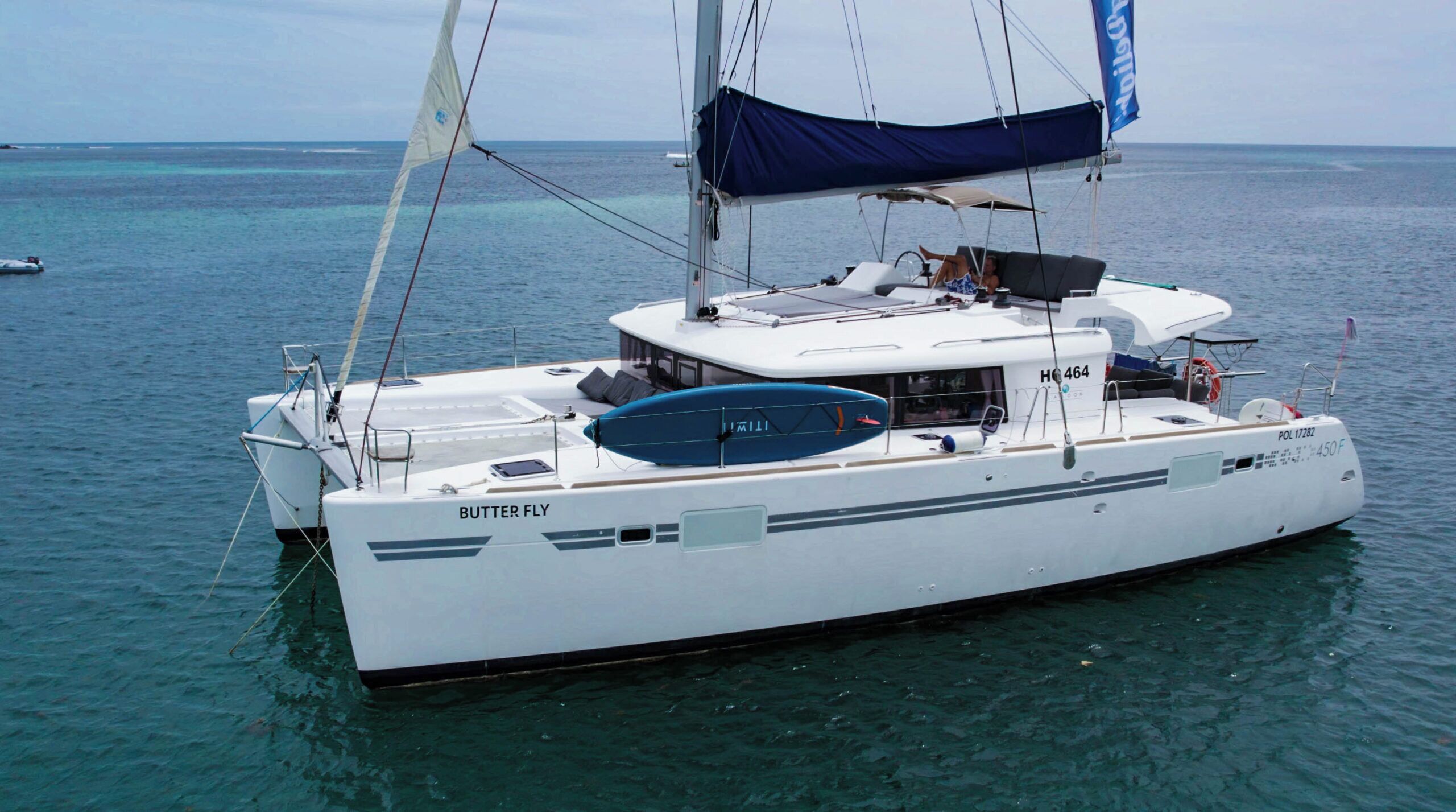 A white sailboat named 'BUTTER FLY' with a cabin, deck seating, and a blue lifebuoy.