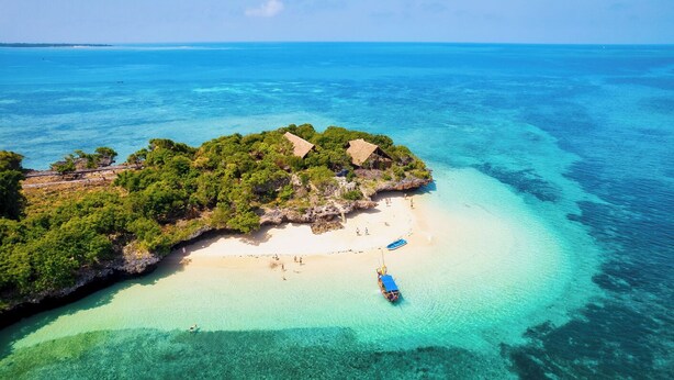 An aerial view of a tropical island with clear turquoise waters, a sandy beach, and a small boat.