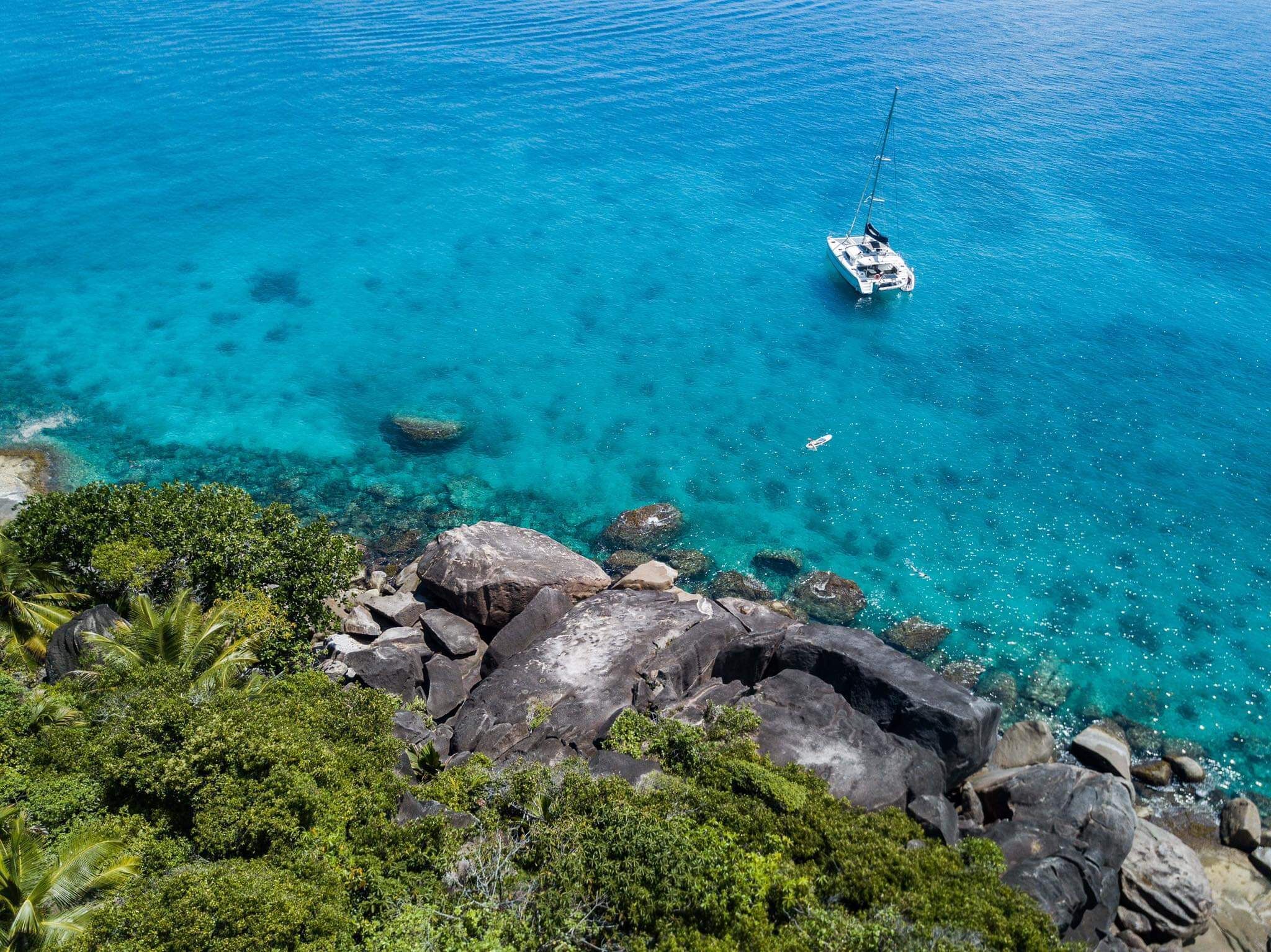 A clear view of a coastal area with a boat anchored in turquoise waters, surrounded by rocky terrain and lush greenery.