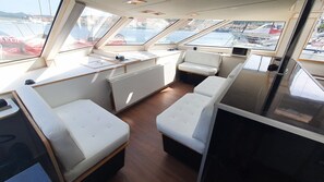 A boat interior with seating, a small table, and a view of the marina. - Sun-kissed Sailing Adventure in Split-Dalmatia, Croatia (Trogir)