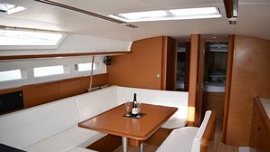 Interior de iate com mesa de madeira, assentos acolchoados brancos e um claraboia.