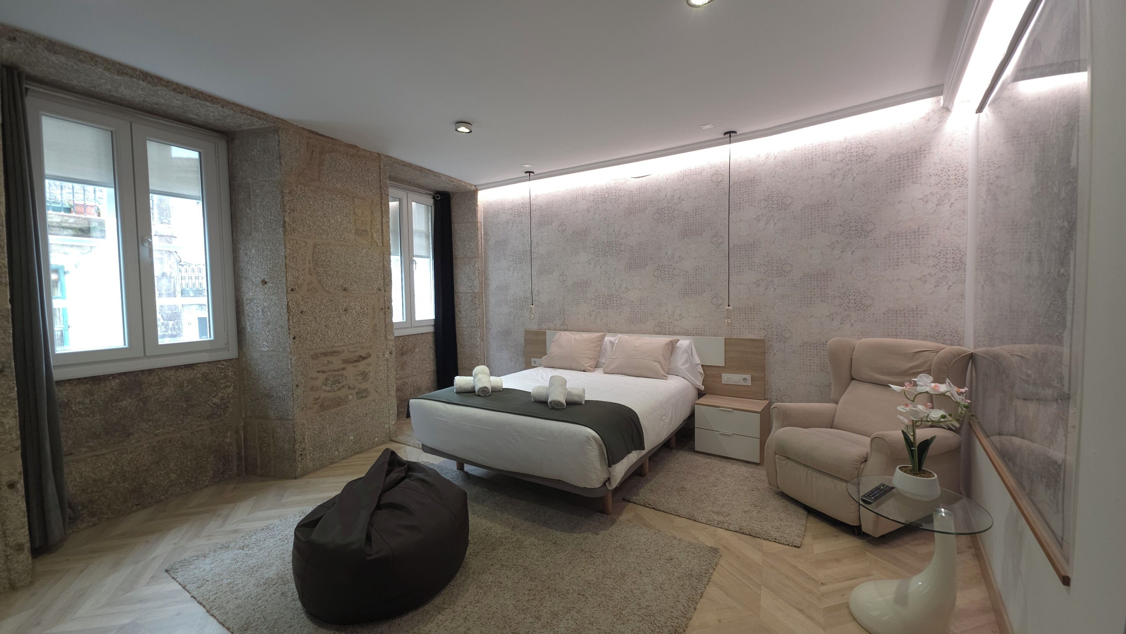 A modern bedroom with a bed, bedside tables, a bean bag, a chair, and a vase with flowers.