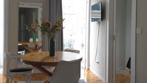 Un comedor con mesa de madera, sillas, un jarrón con flores, una lámpara colgante y un televisor en la pared.