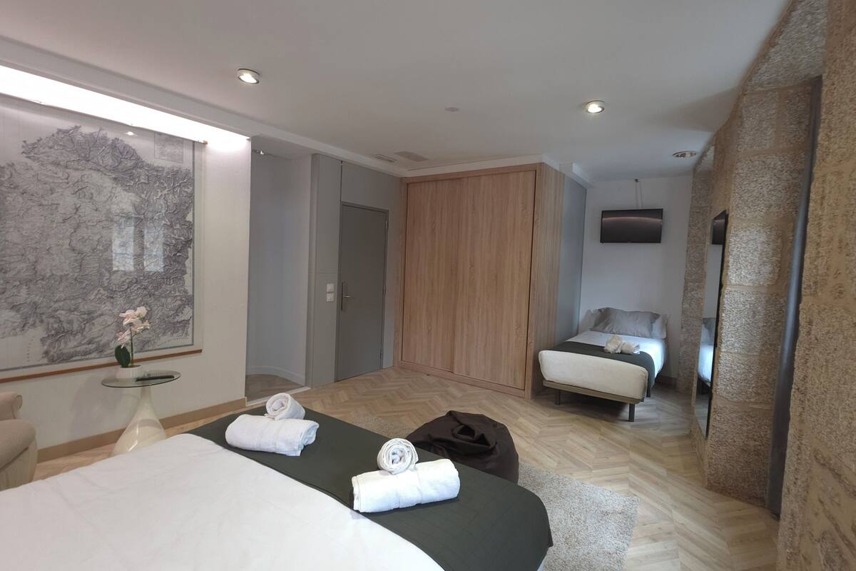 A hotel room with a large bed, a smaller bed, a wardrobe, a mirror, and a wall-mounted TV.