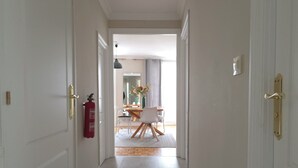 Un pasillo con puertas blancas, un extintor y una zona de comedor al fondo.