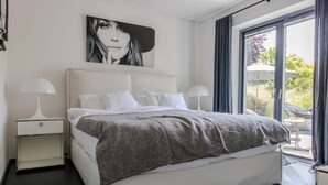 Un dormitorio moderno con una cama grande, dos mesitas de noche, una lámpara de noche, una ventana con cortinas y vistas al exterior.
