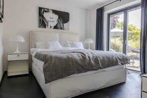 Ein modernes Schlafzimmer mit einem großen Bett, zwei Nachttischen, einem Fenster mit Vorhängen und Blick ins Freie.