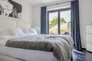 A modern hotel room with a large bed, white bedding, a grey throw, and a view of the outdoors through a sliding door. - Luxuriöses Ferienhaus Room No. 27A (Tating)