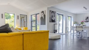 Una sala de estar moderna con un sofá amarillo, un tapete redondo blanco y un comedor con una mesa y sillas blancas.