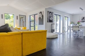 Ein modernes Wohnzimmer mit einem gelben Sofa, einem weißen runden Teppich und einem Essbereich mit einem weißen Tisch und Stühlen.