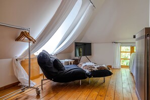 Une pièce avec un plafond en pente, une chaise noire, un pouf recouvert de fourrure, un cintre en bois et un radiateur.