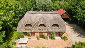 Ein Haus mit einem Reetdach und einem Backsteingrundstück, umgeben von üppiger Bepflanzung.