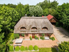 Ein Haus mit einem Reetdach und einem Backsteingrundstück, umgeben von üppiger Bepflanzung.