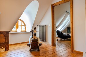 A room with a sloped ceiling, a wooden floor, a radiator, a rocking horse, and a chair. - Luxuriöses Ferienhaus Room No. 7 (Tating)