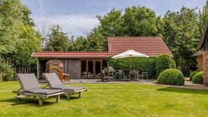 Ein Garten mit zwei Liegestühlen, einem Grill, einem Esstisch mit Stühlen und einer überdachten Terrasse.