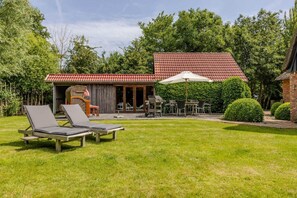 Ein Garten mit zwei Liegestühlen, einem Grill, einem Esstisch mit Stühlen und einer überdachten Terrasse.