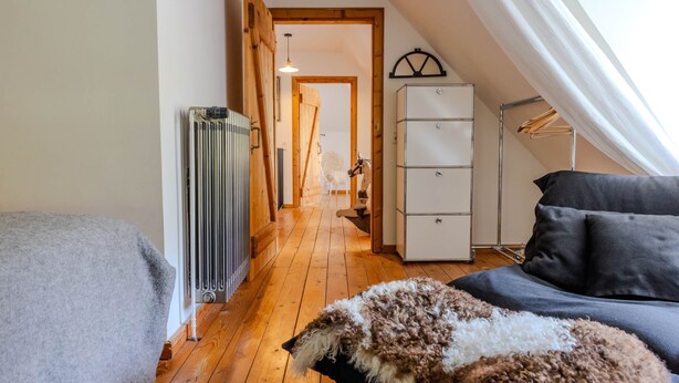 Ein Zimmer mit einem Bett, einem Heizkörper, einem Kleiderschrank, einer Kleiderstange und einem Fenster mit Vorhängen.