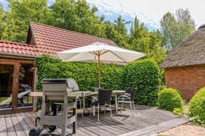 A patio with a grill, outdoor table, chairs, and an umbrella. - Luxuriöses Ferienhaus Room No. 7 (Tating)