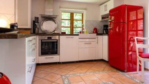 Eine Küche mit weißen Schränken, einem roten Kühlschrank, einem Fenster und einem gefliesten Boden.