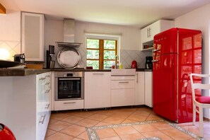 Eine Küche mit weißen Schränken, einem roten Kühlschrank, einem Fenster und einem gefliesten Boden.