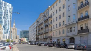 Uma fileira de edifícios altos com varandas, uma rua com carros estacionados e um céu azul límpido.