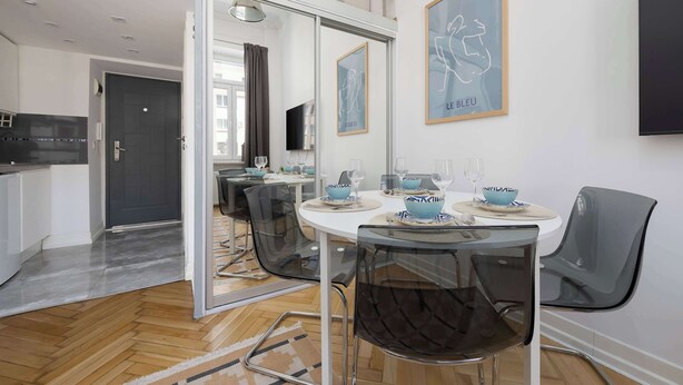 Uma área de refeições moderna com uma mesa de vidro, cadeiras pretas e uma cozinha ao fundo.