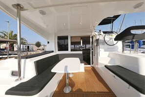 Ein Bootsdeck mit weißem Tisch, gepolsterten Sitzgelegenheiten und einem Steuerrad.