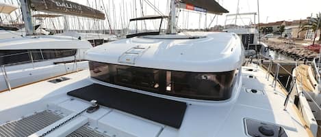 A yacht deck with a covered seating area, a mast, and multiple boats in the background.
