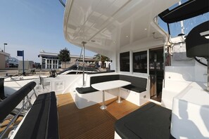 En yachts däck med en sittgrupp, ett bord och utsikt över hamnen.