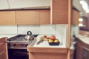A kitchen with wooden cabinets, a stove, and a cutting board with apples. - Sun-Kissed Sailing Adventure in Istria, Croatia (Pula)