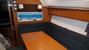 A compact interior with a wooden table, cushioned seating, a painting of a coastal scene, and a wall-mounted clock. - Sun-Kissed Sailing Adventure in the Ionian Islands, Lefkada (Lefkada)