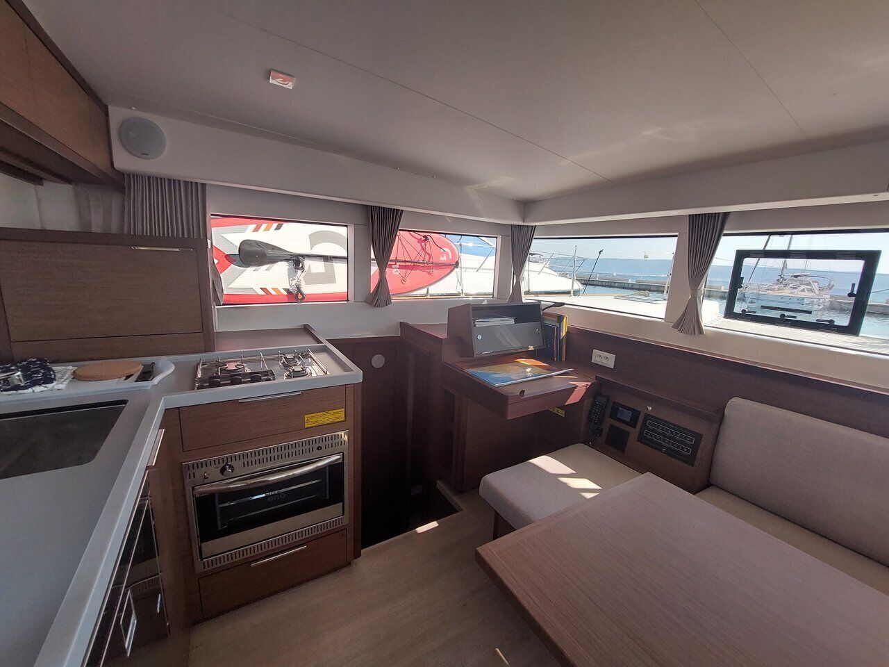 A compact galley with a stove, oven, and sink; a small table with a chair; and a window with a view of the sea.