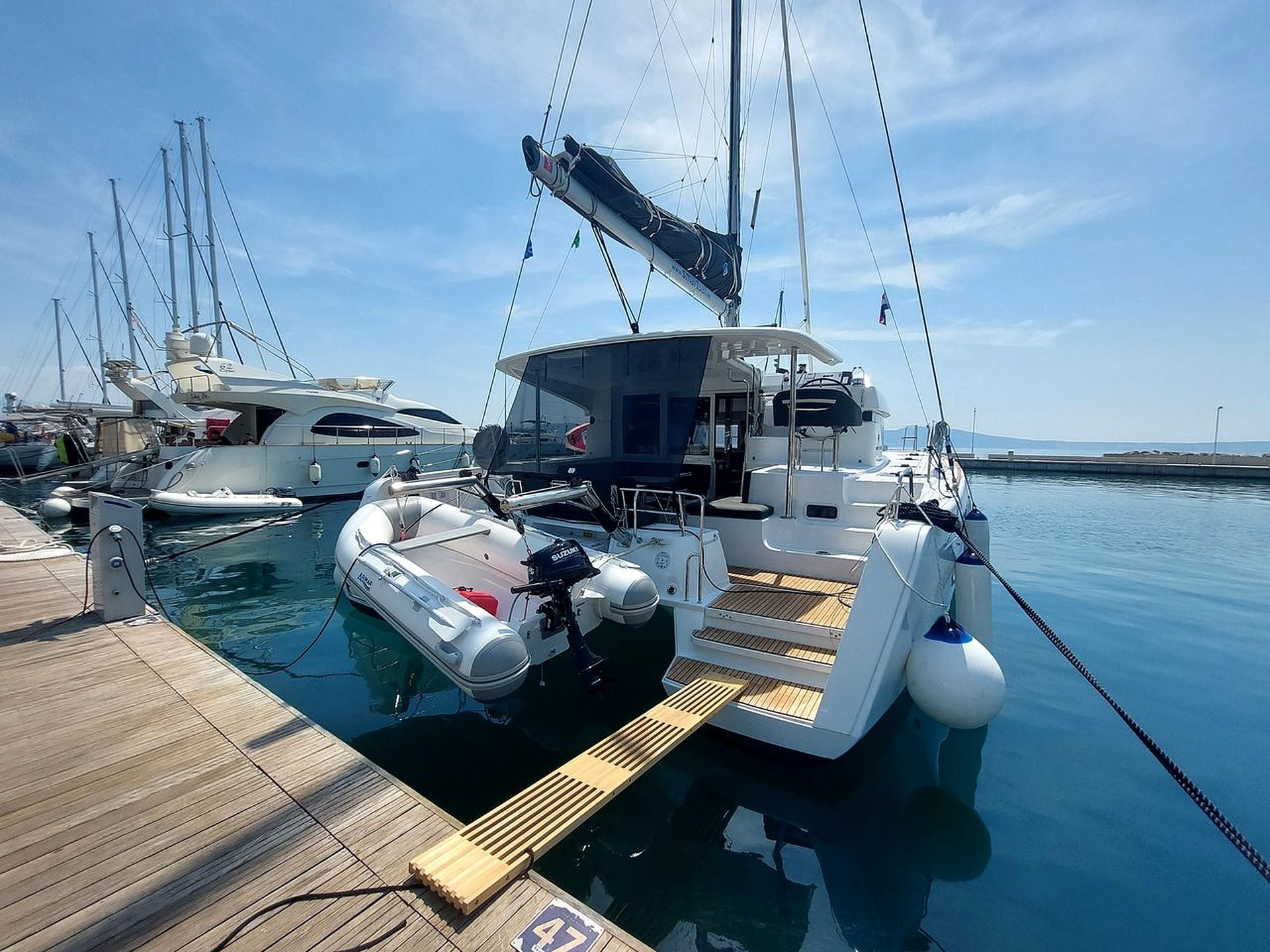 A marina with multiple yachts docked, a wooden deck, and calm water.
