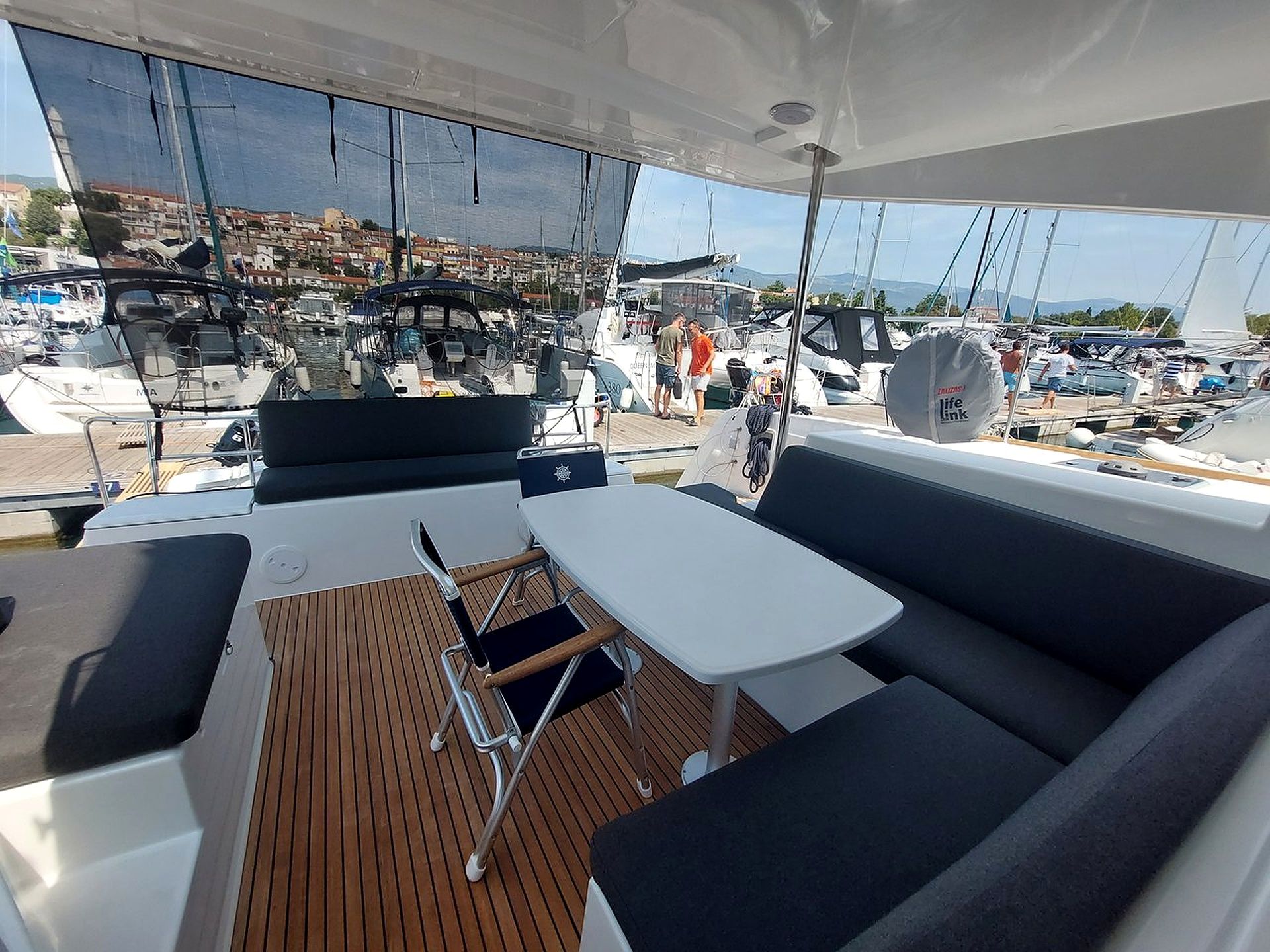 A boat deck with a table and seating area, overlooking a marina with multiple boats.
