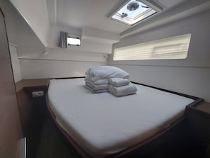 En säng för en person med vita sängkläder, ett takfönster, ett litet fönster och ett nattduksbord.