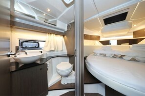 Uma casa de banho compacta para motorhome, com lavatório, sanita e uma cama.