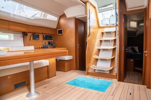 A compact interior with a wooden table, a bench, a small sink, and a storage unit with shelves.