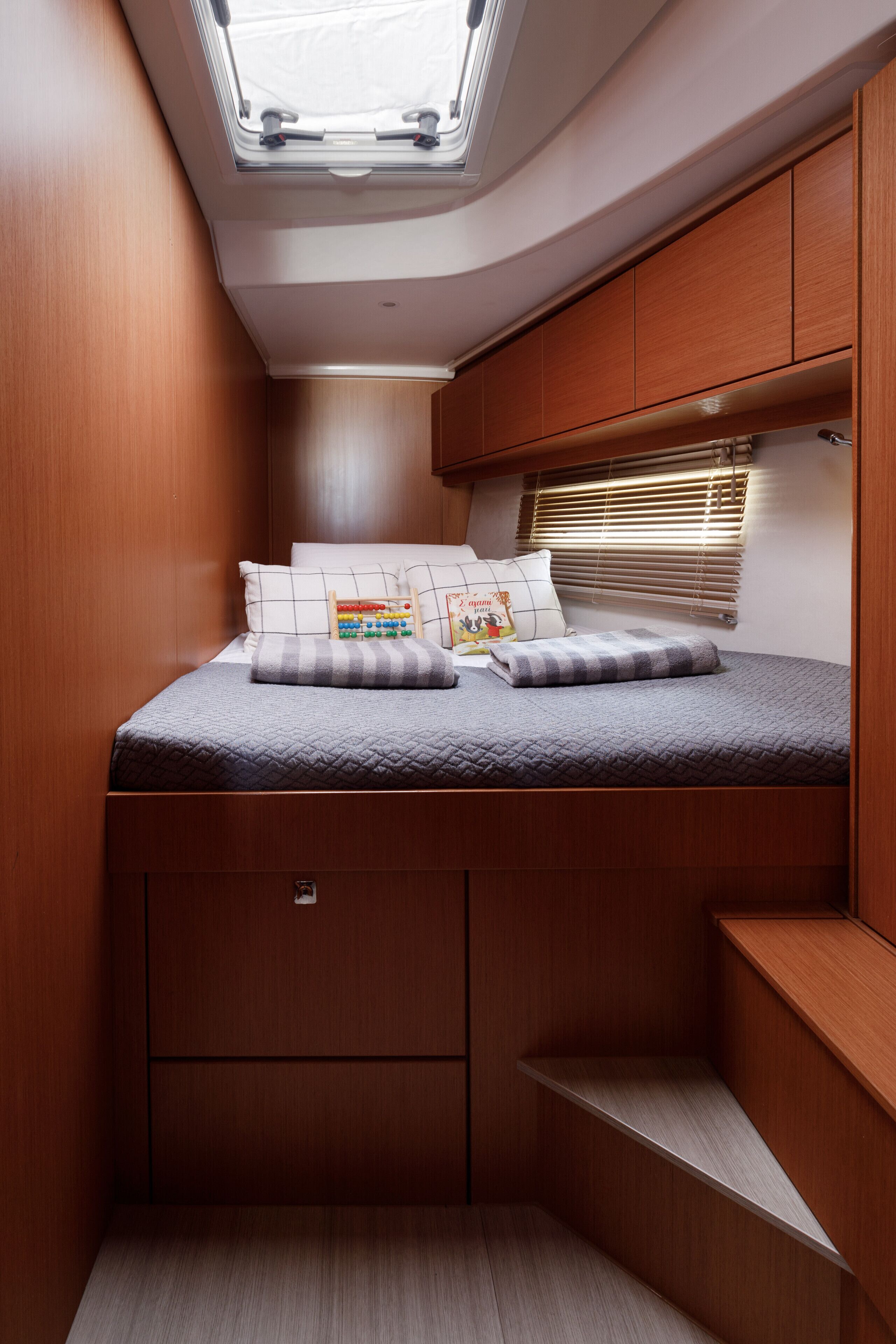 A compact bedroom with a skylight, a bed with pillows, and built-in storage.
