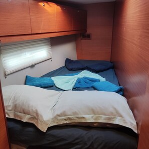 Ein kleiner, kompakter Raum mit einem Einzelbett, einem Fenster mit Jalousien und einem hölzernen Schrank über dem Bett.