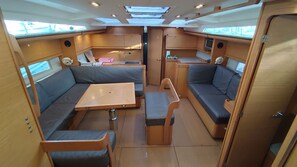 A compact interior with a central table, two seating areas with cushions, a small kitchenette, and a door. - Caribbean Sun-Kissed Sailing: A Luxurious Beach Experience from Martinica, Le Marin (Le Marin)