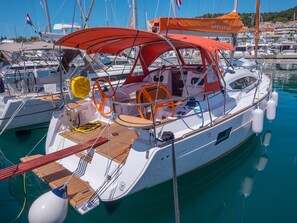 Eine Segelyacht liegt in einer Marina vor Anker, mit einer Kabine, Sitzgelegenheiten auf dem Deck und einem überdachten Bereich.