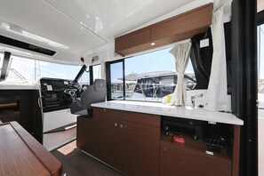 A kitchen area with a counter, sink, and cabinets, a steering wheel, and a window with curtains. - Sun-Kissed Sailing Adventure in Zadar, Croatia (Biograd na moru)