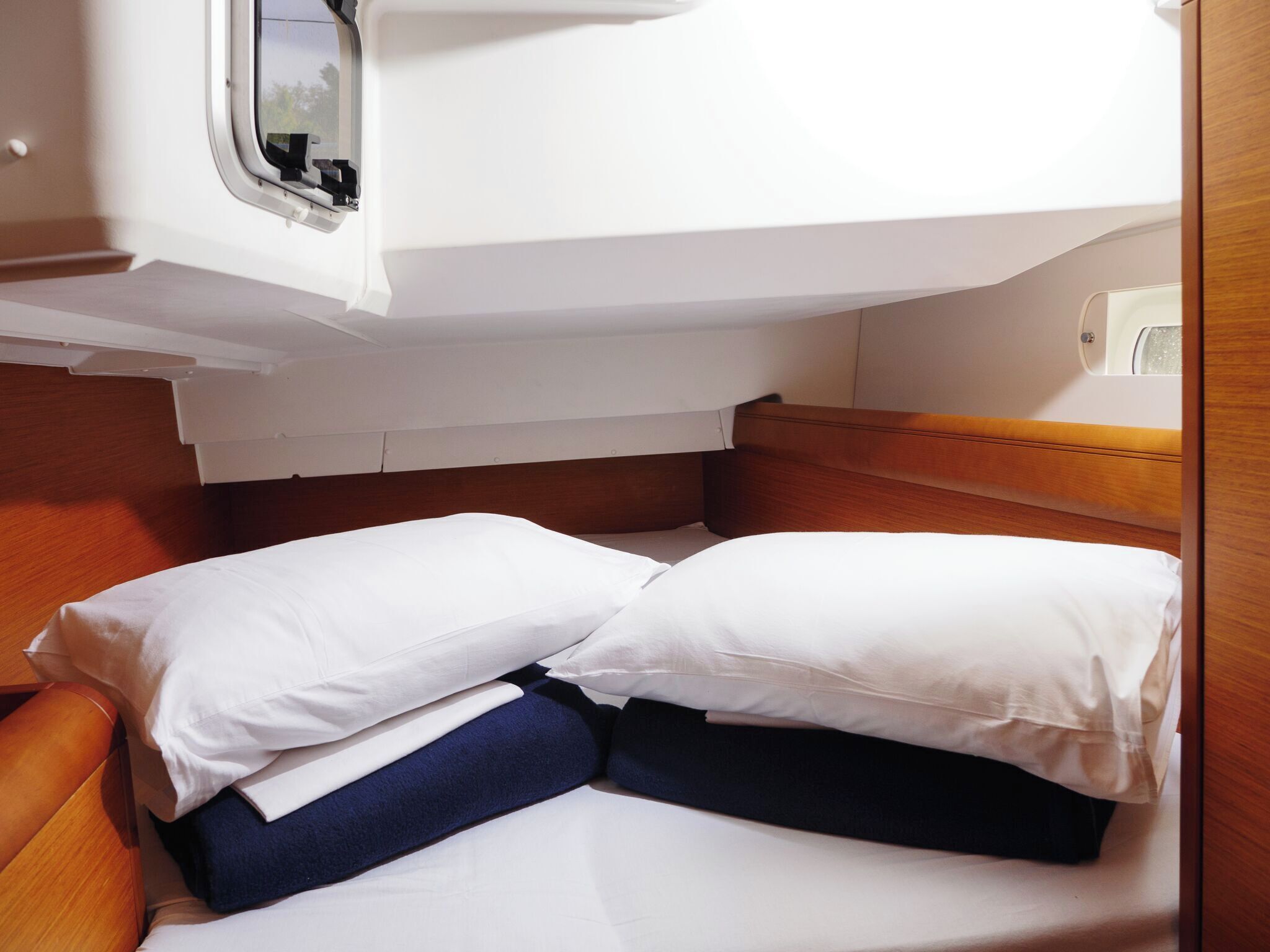 Una cama compacta con ropa de cama blanca y azul oscuro, un cabecero de madera y una ventana arriba.