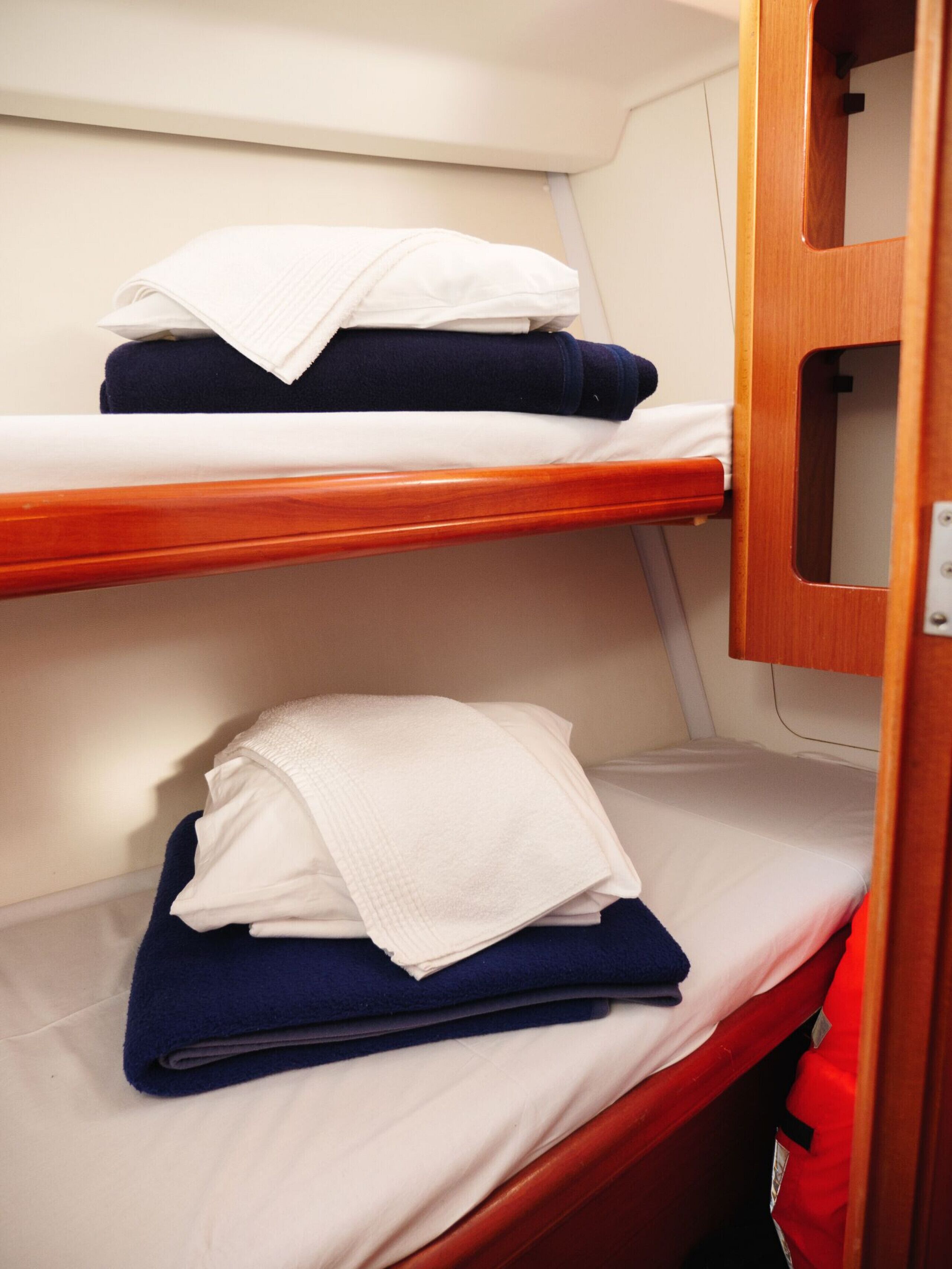Un lit superposé avec une literie blanche et bleu marine, une tête de lit en bois et une petite armoire en bois.
