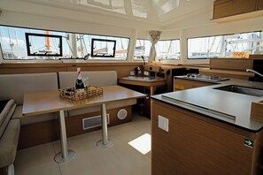 Jachtinnenraum mit Essbereich, Küche und Fenstern, die Segelboote zeigen.