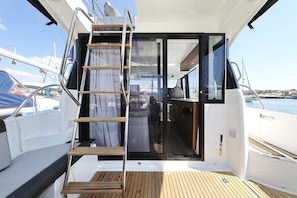 A boat deck with a wooden deck, a ladder leading to an enclosed area, and a view of the marina. - Sibenik Sun-soaked Sailing: A Luxurious Croatian Voyage (Pirovac)