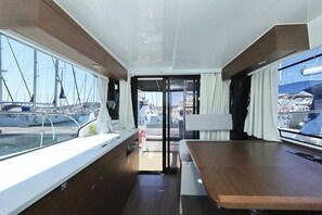 A yacht interior with a dining area, a view of the marina, and a sliding door leading to the deck. - Sibenik Sun-soaked Sailing: A Luxurious Croatian Voyage (Pirovac)