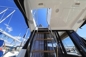 Schiffsinnenraum mit einer Leiter, die zu einem Deck führt, freie Sicht auf den Himmel und andere Boote im Hintergrund.