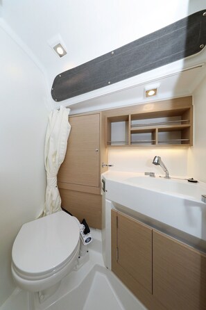 Ein kleines Badezimmer mit Toilette, Waschbecken mit Chromarmatur und Holzschränken.