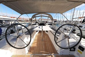 Coixinet del vaixell amb dos timons, un pont de fusta i un port esportiu amb altres vaixells al fons.